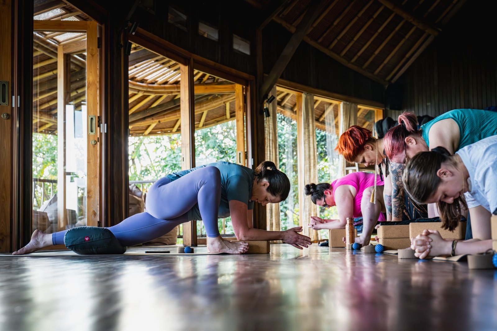 A group of women practising yoga in a wooden open-air studio surrounded by nature at a Bali wellness retreat.